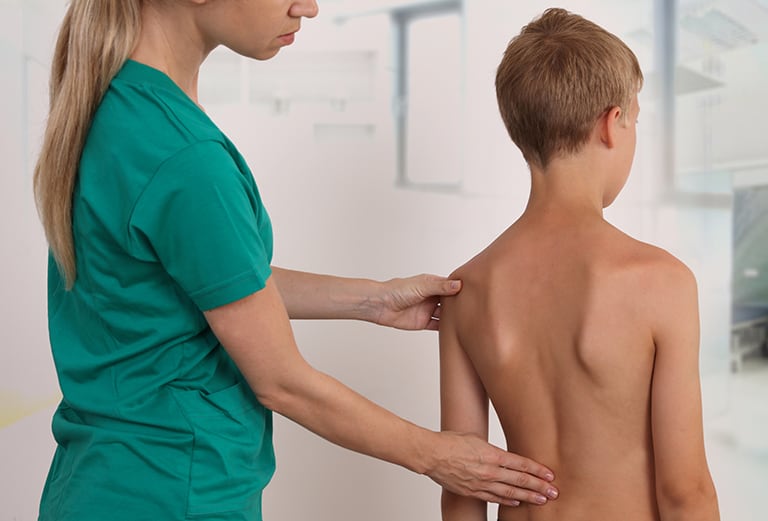 Chiropractor examining the back of a child who is standing.