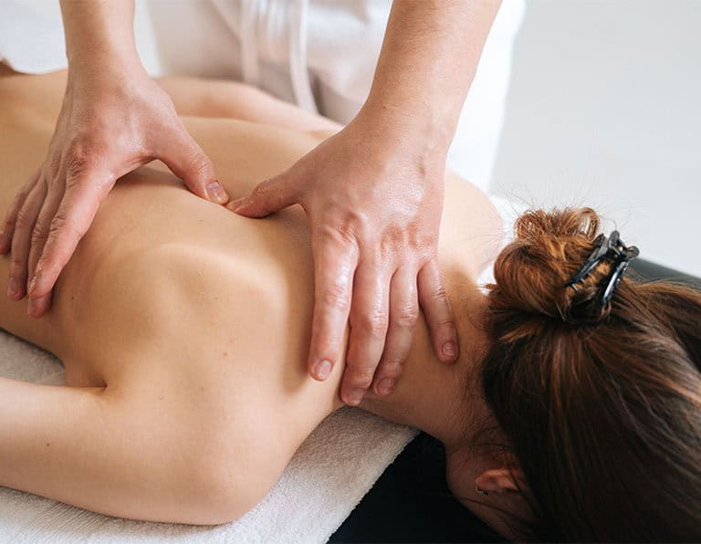 Person facing down on a table while massage hands press down near the shoulder blades.